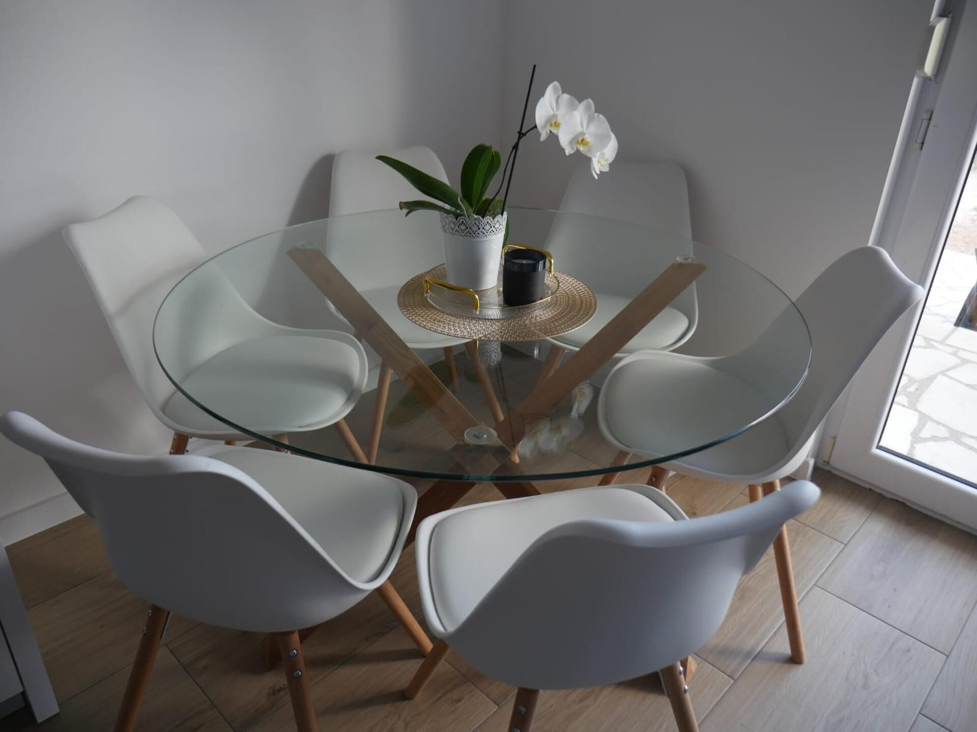Une table ronde en verre, entourée de chaises blanches, avec une plante en pot et un petit objet noir posé sur la table.
