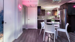 Een moderne keuken met een eethoek, met een neonbord, een wolkplafond en een roestvrijstalen koelkast.