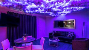 Een kamer met een plafond dat lijkt op een wolk, een bank, een televisie en een eethoek.