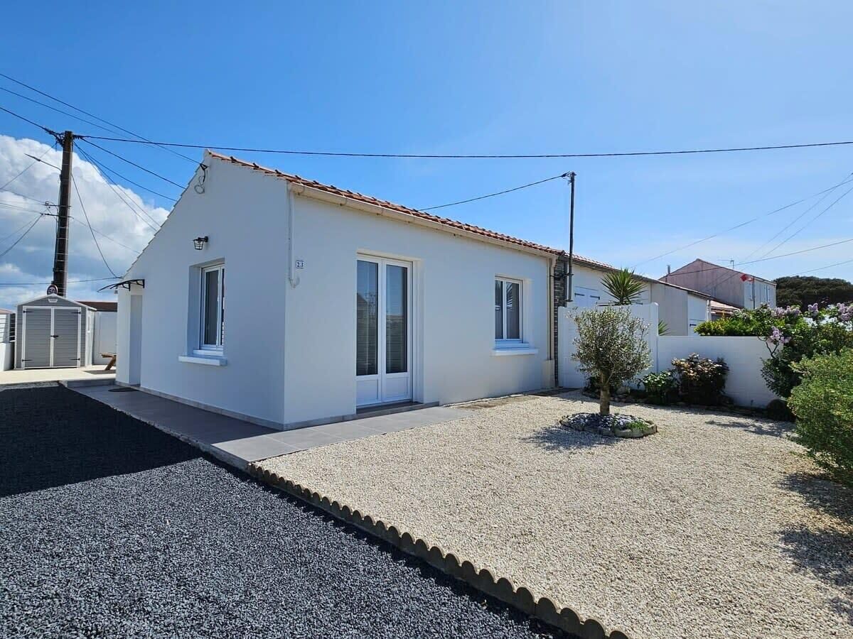 A single-story white building with a tiled roof, a small front yard with gravel and a young tree, and a clear blue sky.