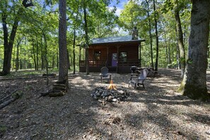 A cabin with a fire pit and Adirondack chairs in a forest setting.