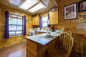 A wooden cabin interior with a kitchen area, including a stove, sink, and a dining table with chairs.