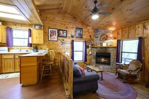 A cozy cabin interior with a stone fireplace, wooden furniture, and a dining area.