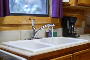 A kitchen sink with a modern faucet, wooden cabinetry, and a window with purple curtains.