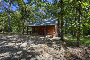 A rustic cabin with a porch, surrounded by trees in a wooded area.
