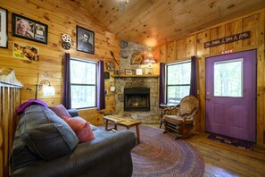 A cozy cabin interior with a fireplace, wooden walls, a leather sofa, and a rocking chair.
