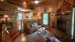 Un accogliente interno di una baita con camino, pavimento in legno, un divano e zona pranzo.