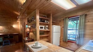 Interno di una baita in legno con angolo cottura, un tavolo da pranzo e due tazze, e un frigorifero.