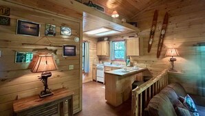 Interno di una baita con cucina, zona pranzo e accogliente angolo living, caratterizzato da pareti e soffitto in legno.