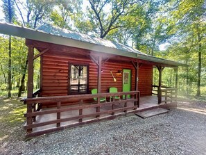 Una cabaña de madera con porche, sillas verdes y un sendero de grava.