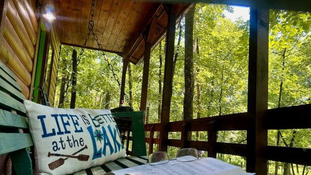 Una panca di legno con un cuscino e un libro, in un'area esterna coperta con vista sugli alberi.
