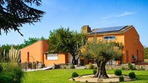 Une maison moderne dotée d’une cheminée en pierre, de panneaux solaires et d’un jardin bien entretenu.