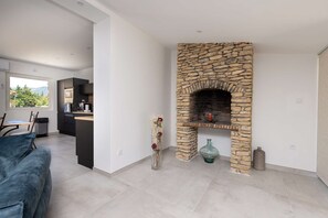 A modern kitchen with a stone fireplace, a dining area with a blue sofa, and a view of the outdoors. - SmartStay P.Cézanne - Proche L'Isle-sur-la-Sorgue (Lagnes)
