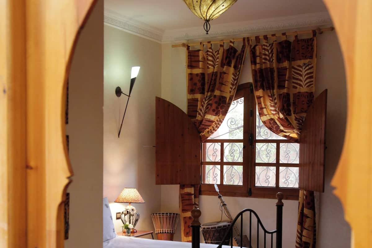 A bedroom with a bed, a window with curtains, a lamp, and a rug.