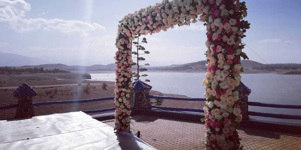 A wedding arch decorated with flowers overlooking a body of water.