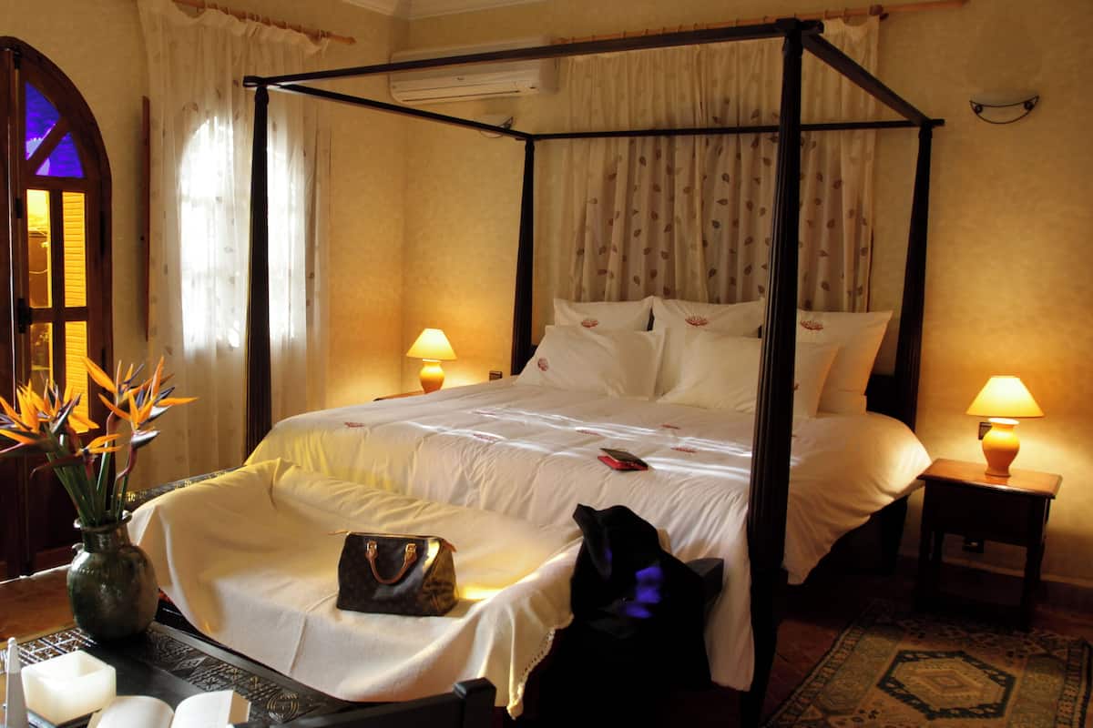 A four-poster bed with white linens, a bedside table with a lamp, and a vase with flowers.