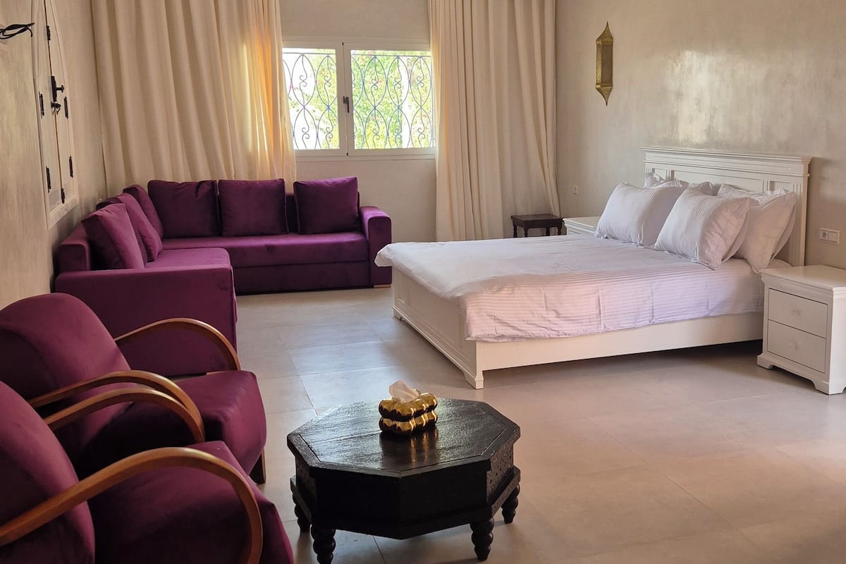 A bedroom with a bed, a purple sofa, a small table, and a chandelier.
