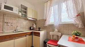 Une cuisine compacte équipée d’un four à micro-ondes, d’un évier et de placards. On y trouve une table à manger avec une chaise et un panier de fruits.