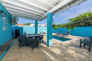 Un espacio al aire libre techado con piscina, asientos y una mesa.