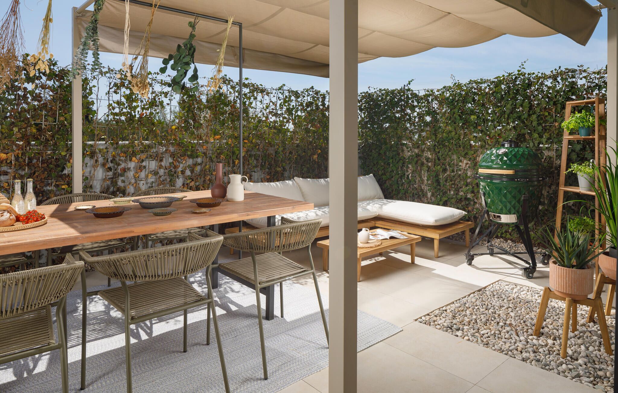 Une terrasse extérieure avec une table en bois, des chaises en osier, un canapé rembourré et un barbecue vert.