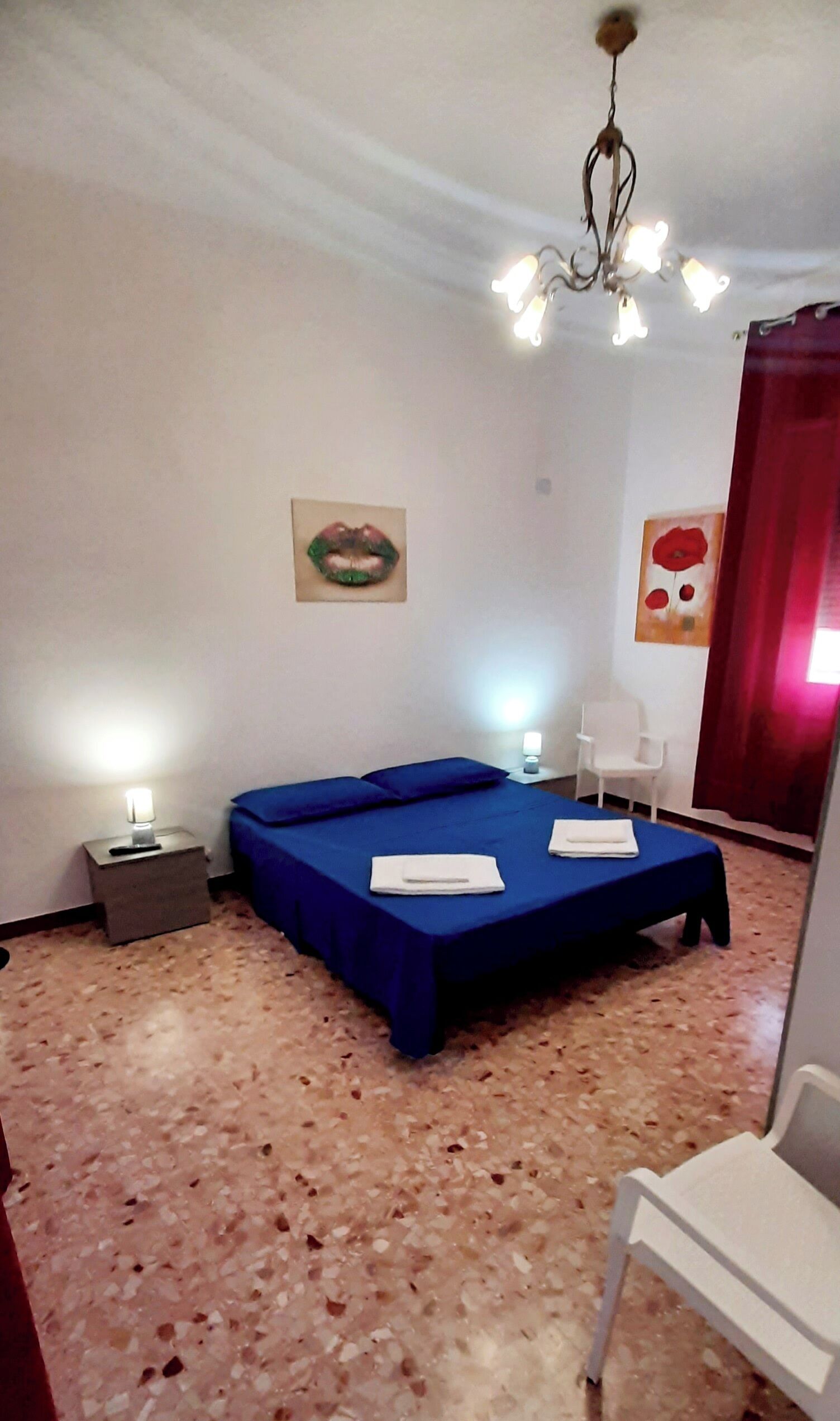 A bedroom with a bed, a chair, a nightstand, and a chandelier.