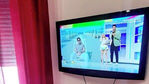 A television mounted on a wall displaying a show with three people. - The house of the islands Sea View ( The House Of The Islands ) (Marausa Lido)