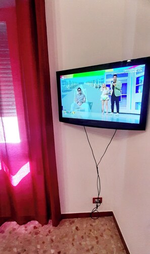 Ein an der Wand befestigter Fernseher zeigt eine Sendung mit drei Personen.