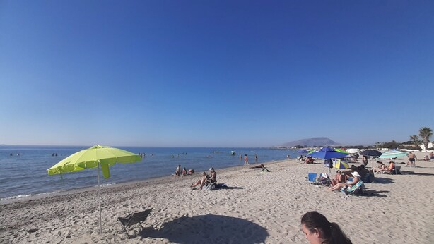 A beach with people sunbathing and swimming, umbrellas, and a clear sky. - The house of the islands Sea View ( The House Of The Islands ) (Marausa Lido)