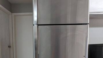 A stainless steel refrigerator in a kitchen with tiled flooring and a white door in the background.
