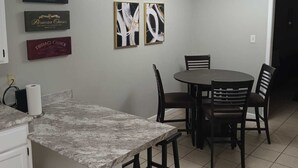 Une cuisine dotée d’un plan de travail en marbre, un coin repas avec une table ronde et des chaises, et des œuvres d’art accrochées au mur.