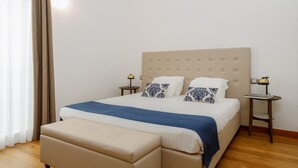 A bedroom with a large bed, two bedside tables with lamps, a window with curtains, and a wooden floor.