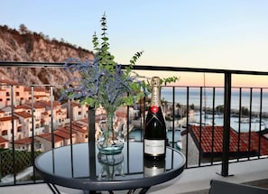 Een glazen tafel met een fles Moët & Chandon champagne en een bloemenvaas op een balkon met uitzicht op een kustplaats.