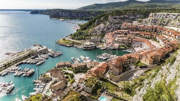 A coastal town with a marina, terraced buildings, and a mountainous backdrop.
