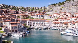 A coastal town with a marina, terraced buildings, and a rocky hillside.