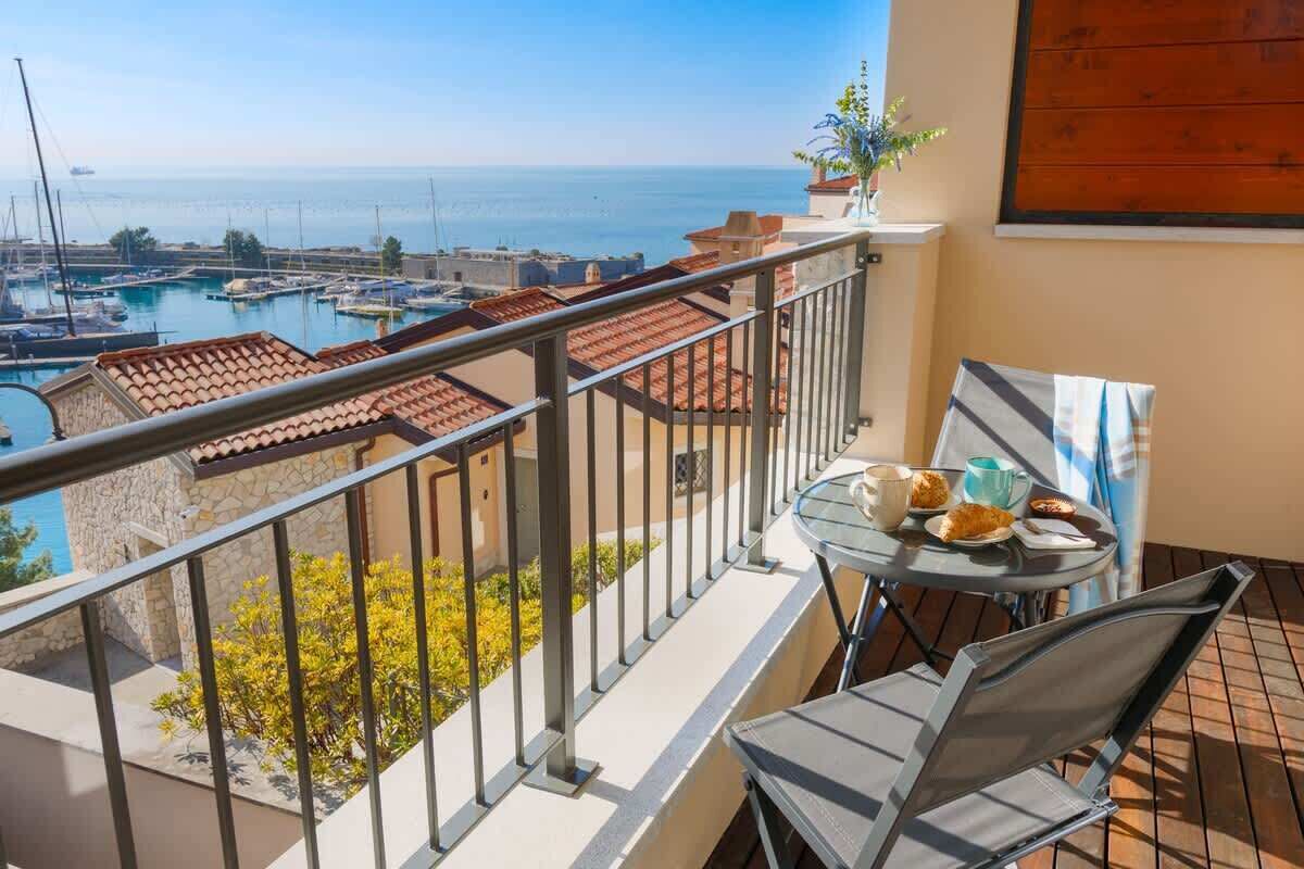 Ein Balkon mit Tisch und Stühlen, der auf einen Yachthafen und das Meer blickt.