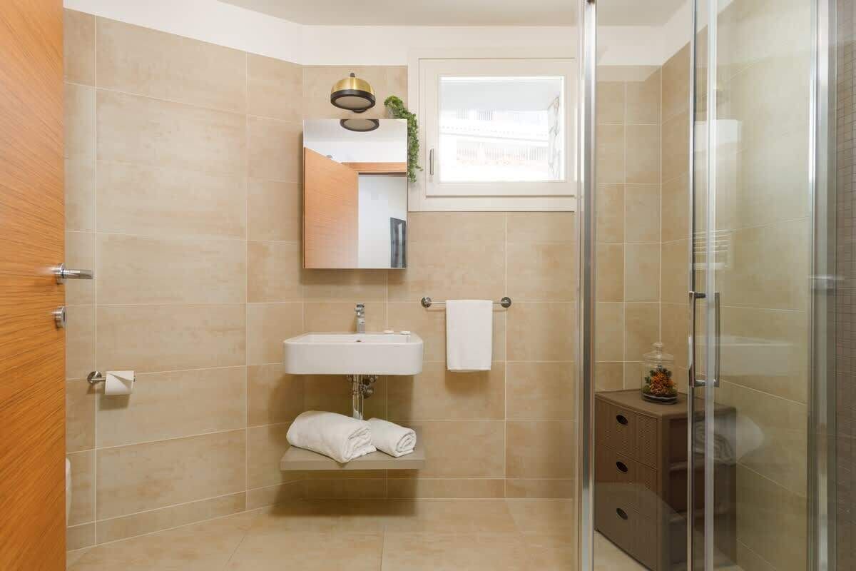 A bathroom with a glass shower enclosure, a sink, a mirror, and a towel rack.