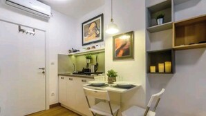 Une cuisine compacte avec des meubles blancs, un coin repas comprenant une petite table et des chaises, et une étagère murale agrémentée d’objets décoratifs.
