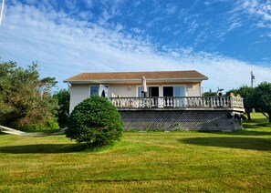 Ein zweigeschossiges Haus mit Balkon, umgeben von einem gepflegten Rasen und Bäumen.