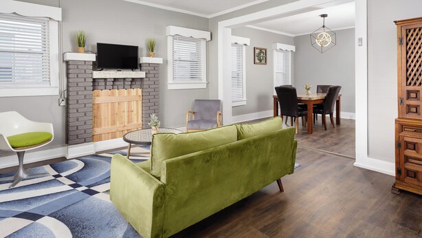 A living room with a green sofa, a fireplace, a TV, and a dining area with a table and chairs. - Charming 4-bedroom 3bath house in terrific Florence with WiFi, AC (Florence)