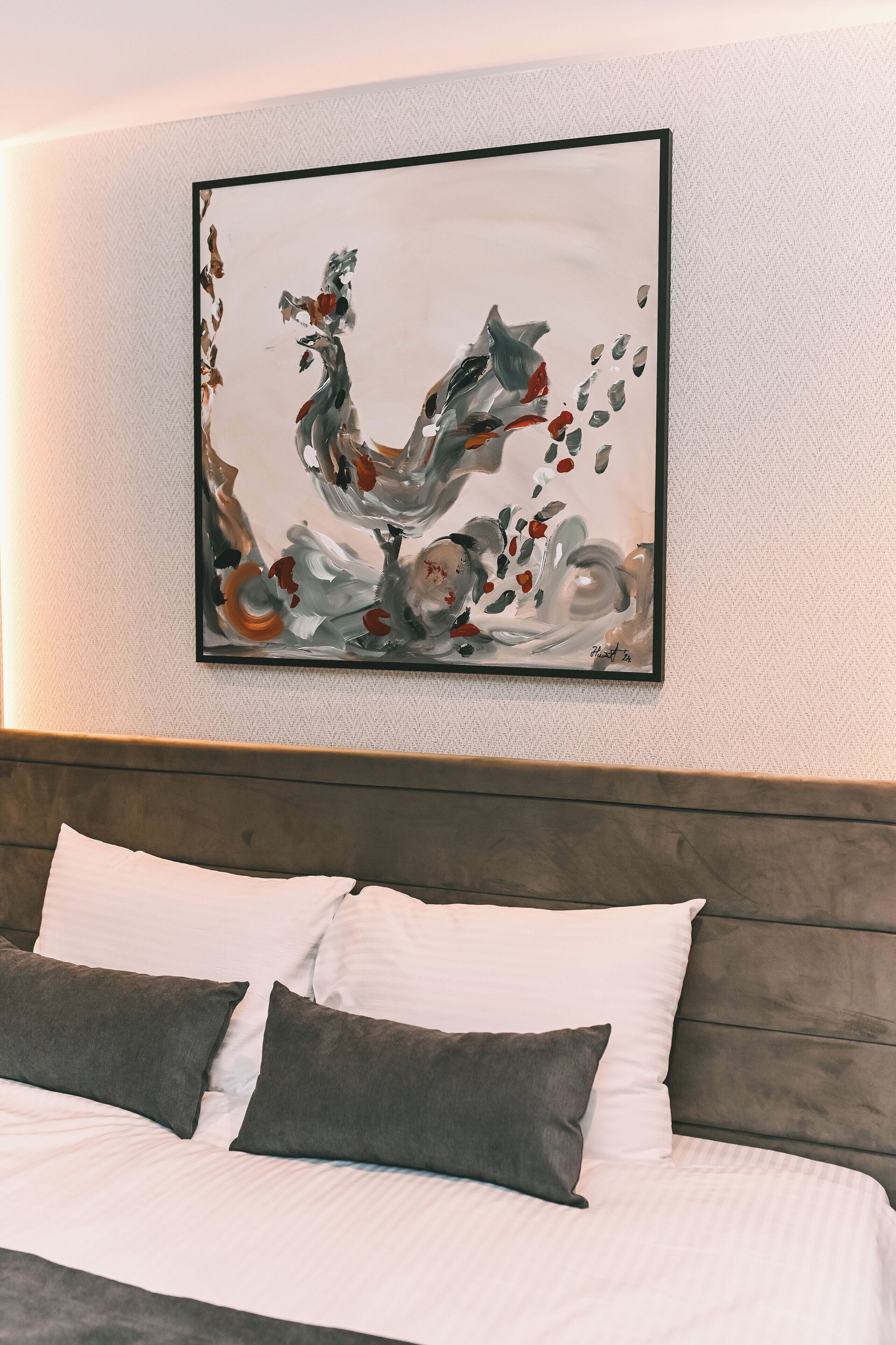 Una habitación de hotel moderna con un cuadro abstracto grande en la pared, una cama bien hecha con ropa de cama blanca y gris, y un cabecero de madera.