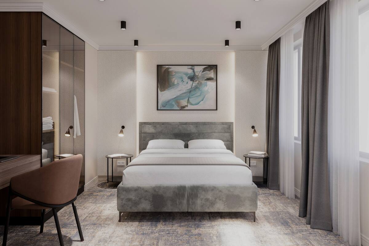 Ein modernes Hotelzimmer mit einem großen Bett, einem Schreibtisch und einem Stuhl. Es gibt zwei Nachttische und ein großes Fenster mit Vorhängen.
