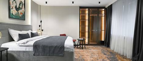 A modern hotel room with a large bed, a small table, a chair, a nightstand, and a large window with curtains.