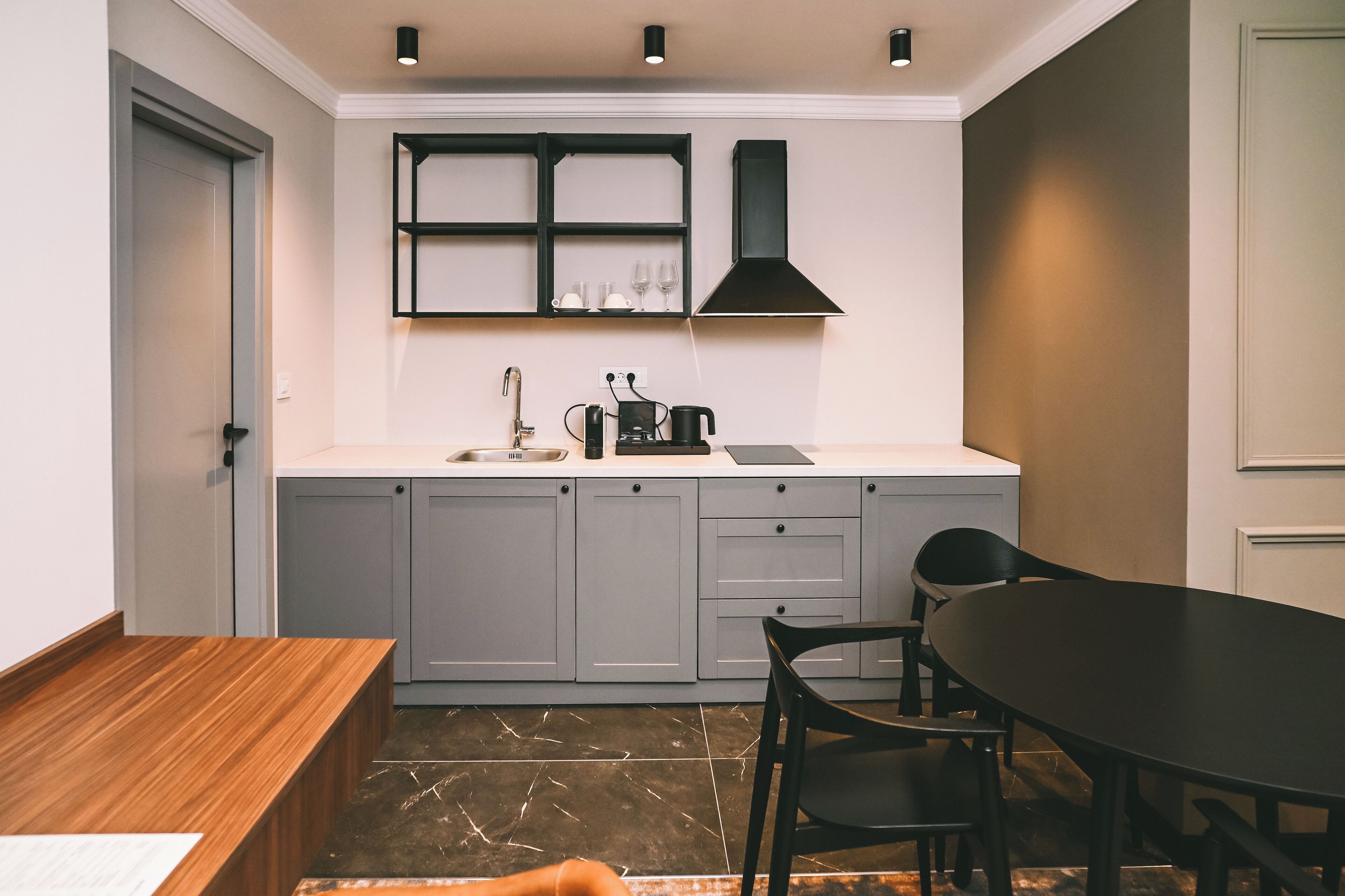 Een moderne keuken met grijze kastjes, een zwart aanrecht en een zwarte eettafel met stoelen.