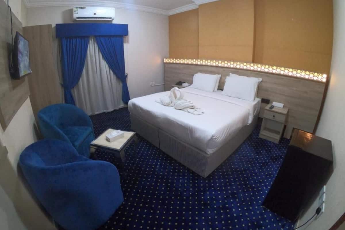 A hotel room with a bed, a desk, a chair, an air conditioning unit, and a television.