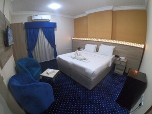 Habitación de hotel con cama, escritorio, silla, aire acondicionado y televisor.