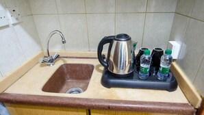 Une cuisine équipée d’un évier, d’une bouilloire et de deux bouteilles d’eau posées sur un plan de travail.