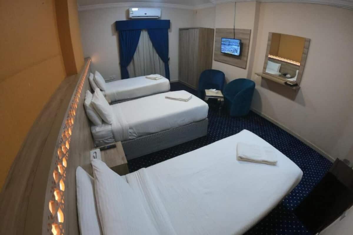 A hotel room with two single beds, a desk, a chair, a TV, and a mirror.