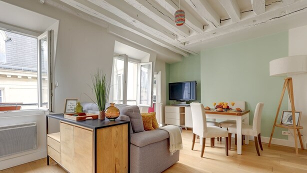 A modern living room with a grey sofa, wooden sideboard, and a dining area with a white table and chairs.