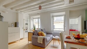 A modern living room with a grey sofa, a dining table with breakfast, and a kitchen in the background.