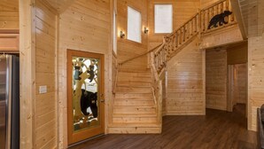 Un intérieur en bois avec un escalier, une porte en verre ornée de motifs d’ours et la silhouette d’un ours sur la rambarde.